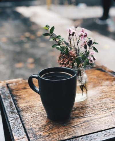 A cozy coffee cup beside a small vase of flowers on a wooden table, creating a warm and inviting atmosphere.