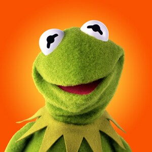 A cheerful green puppet with large eyes and a friendly smile against a vibrant orange background, symbolizing fun and creativity.