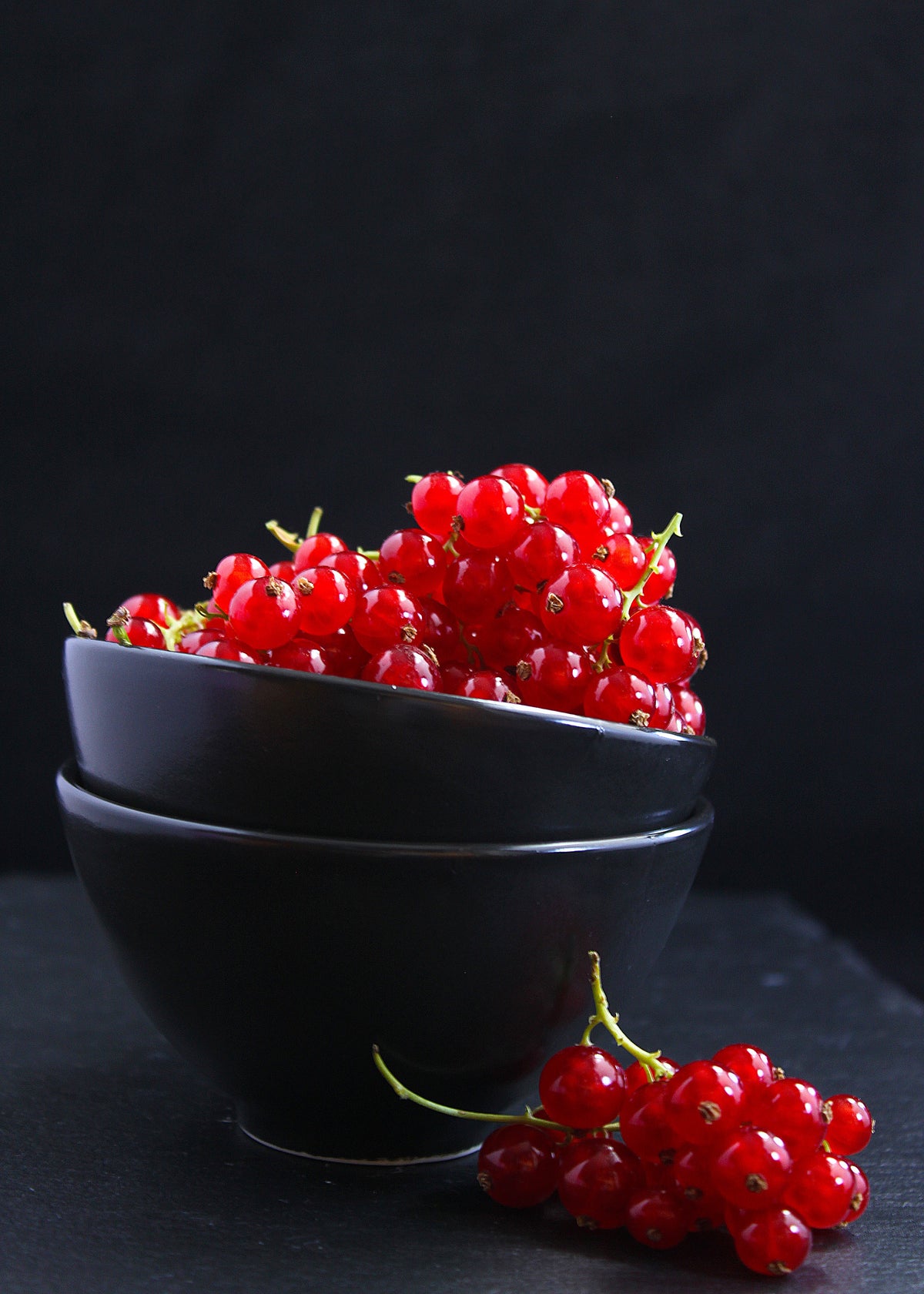 Fresh red currants piled in black bowls against a dark background, showcasing their vibrant color and juicy texture.